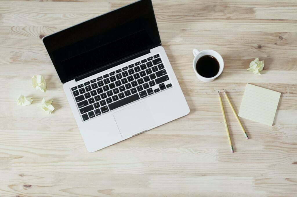 Laptop on a wooden surface with pencils, paper and coffee