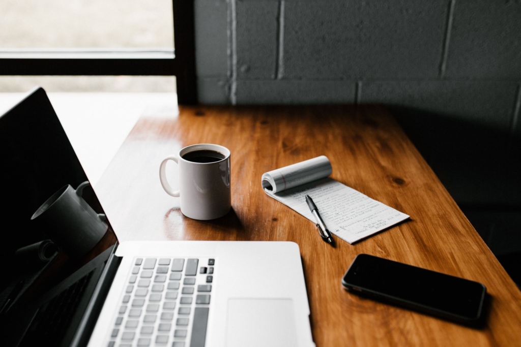 Laptop on a table with a mug of coffee, notepad and mobile phone