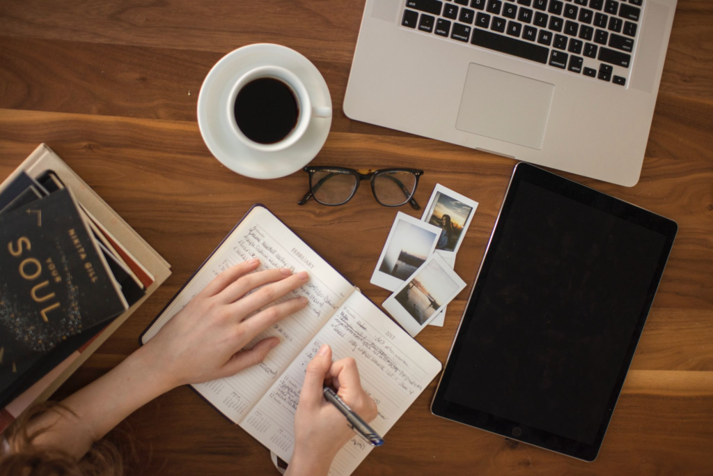 Woman writing in a notebook on a table with a tablet, books and a laptop