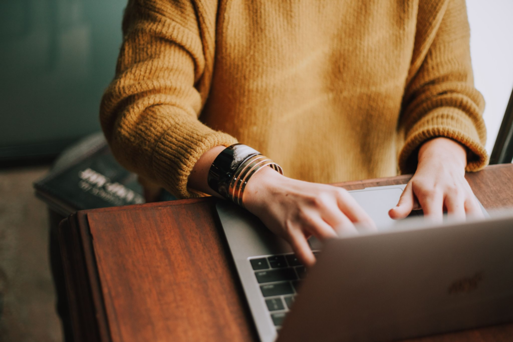 Person in yellow jumper writing a blog on a laptop